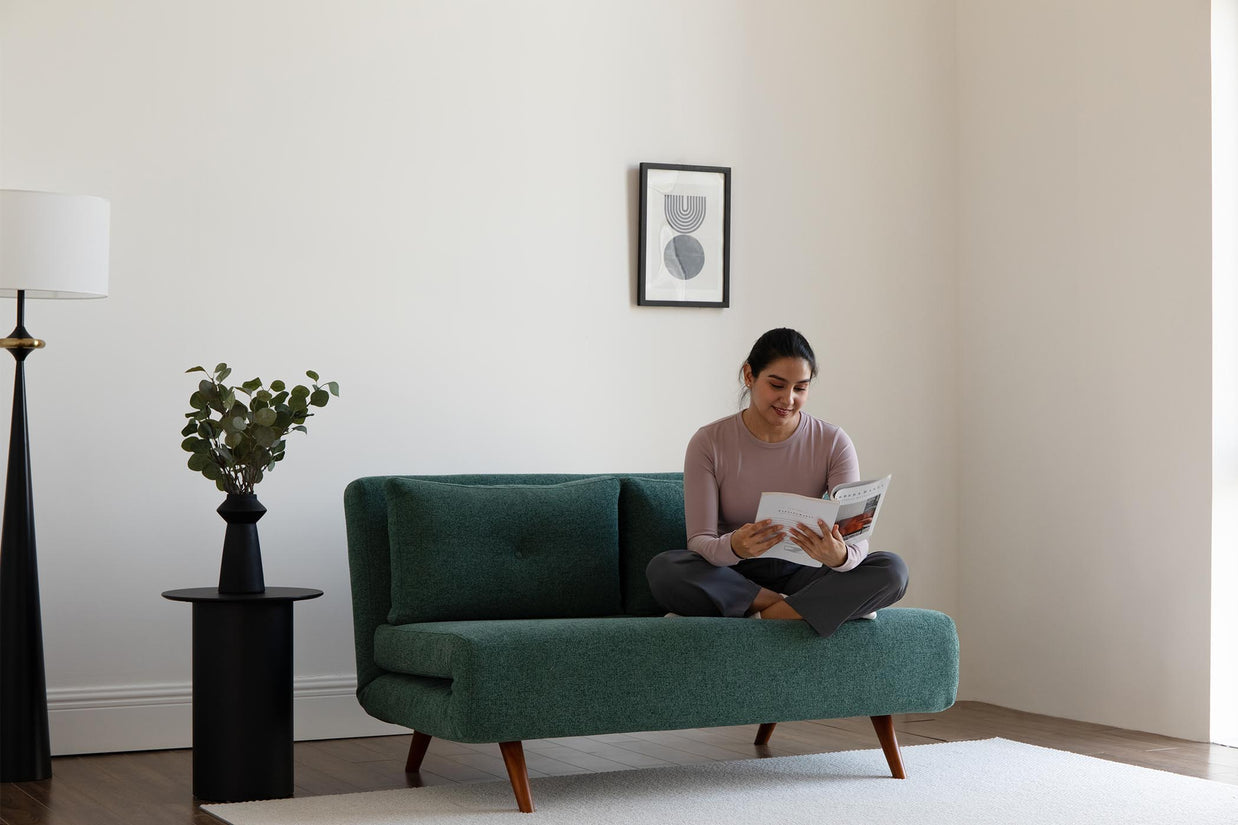 model sitting on sofa bed, reading a book.