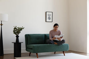 model sitting on sofa bed, reading a book.